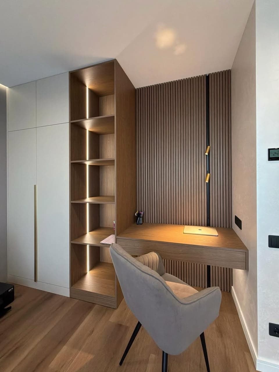 Study nook with a floating desk, backlit wood shelving and slatted wall panelling beside a fitted wardrobe